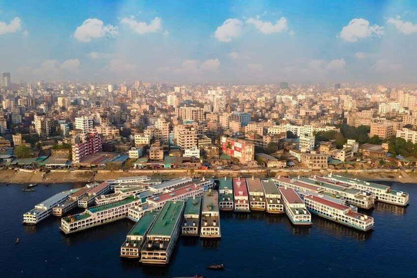 A river with several boats docked along the shore, a cityscape in the background, and a clear sky. 3