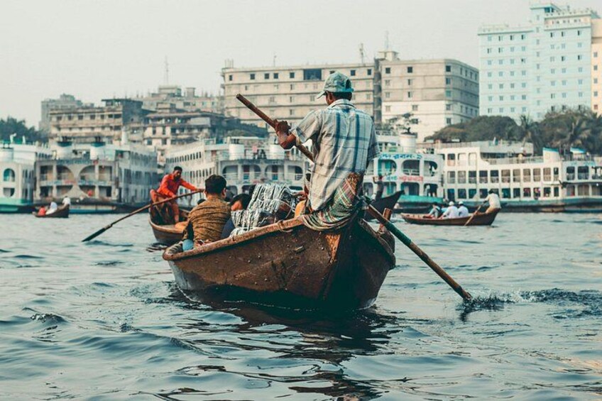 A man rowing a boat with passengers, with buildings in the background. 4