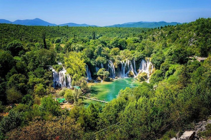 A waterfall cascading into a turquoise pool surrounded by dense green forest and distant mountains. 1
