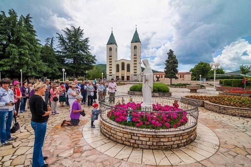 A public square with a central statue, a church with two towers, and a crowd of people. 2