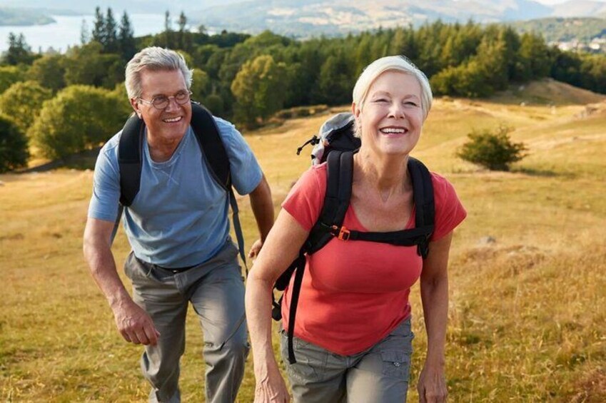 Twee mensen wandelen over een grasland met bomen en heuvels op de achtergrond. 2