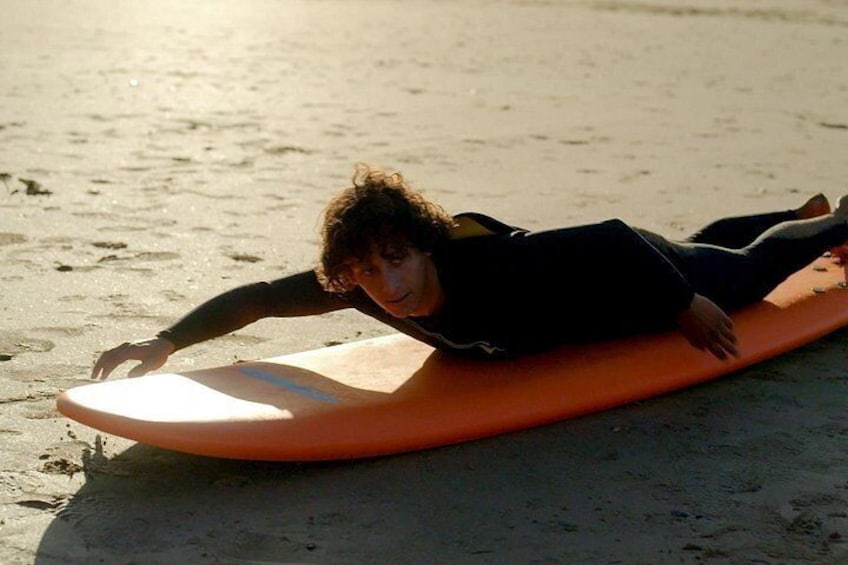 A person lying on a surfboard on a sandy beach. 5