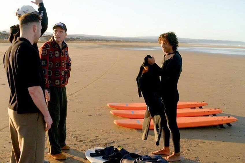 A beach with people standing and a surfboard. 1