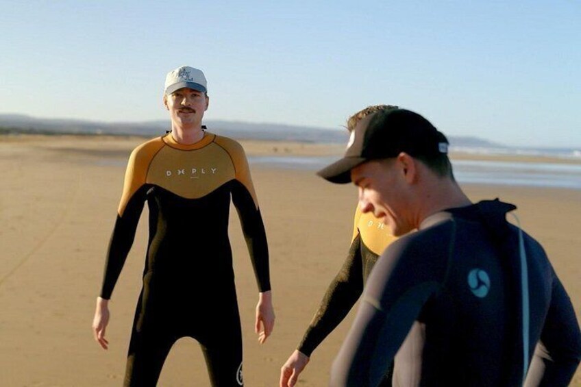 Two people on a beach, one in a wetsuit and the other in a cap. 3