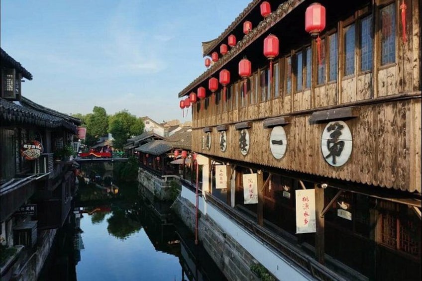 Un edificio tradizionale in legno, con lanterne rosse e caratteri cinesi, un canale stretto e un veicolo rosso sullo sfondo. 4