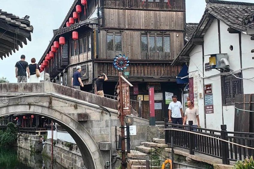 Un ponte in pietra con persone che lo attraversano, edifici tradizionali in legno con lanterne rosse e un cartello. 3