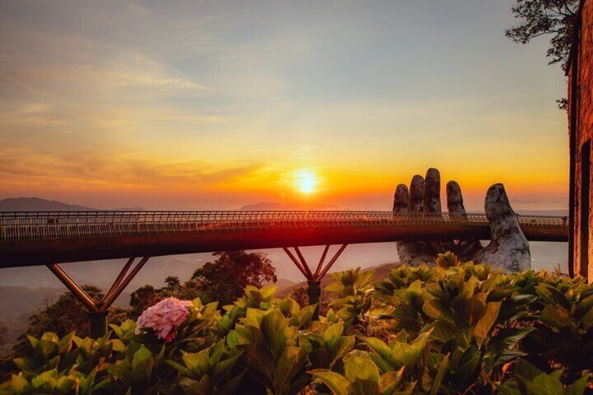 Een brug met een unieke handbeeld, weelderige begroeiing en een zonsondergang. 3