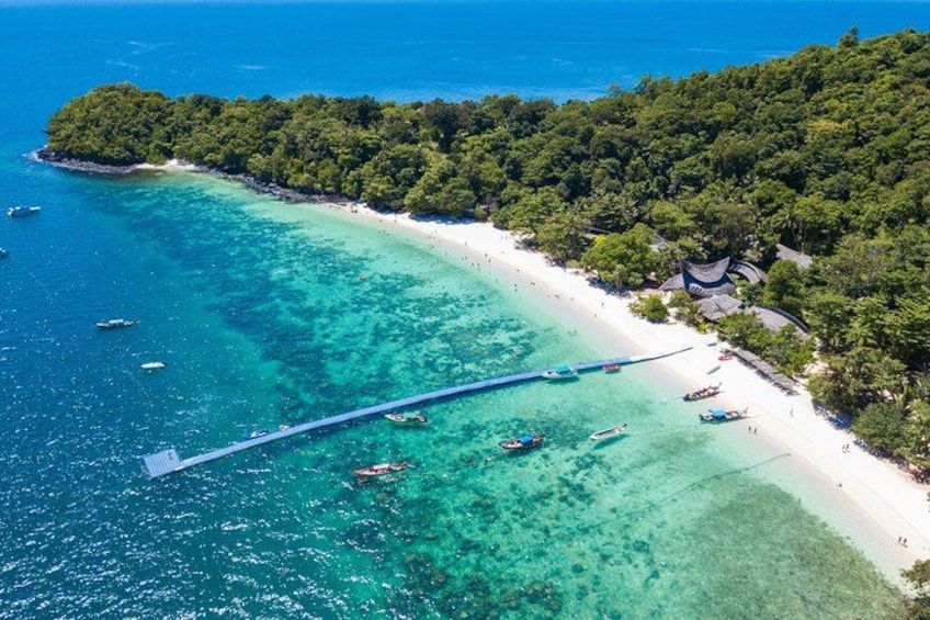 A tropical beach with clear turquoise waters, a wooden pier, and a small island with dense greenery. 1