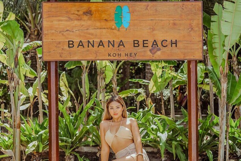 A wooden sign with the text 'BANANA BEACH KOH HEY' and a tropical background with banana plants. 3