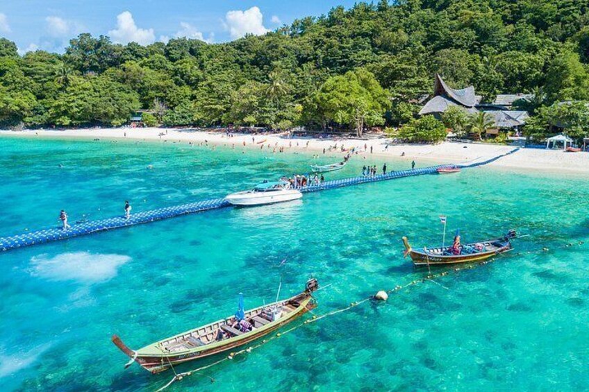 A tropical beach with clear turquoise waters, a wooden walkway, and traditional boats. 1