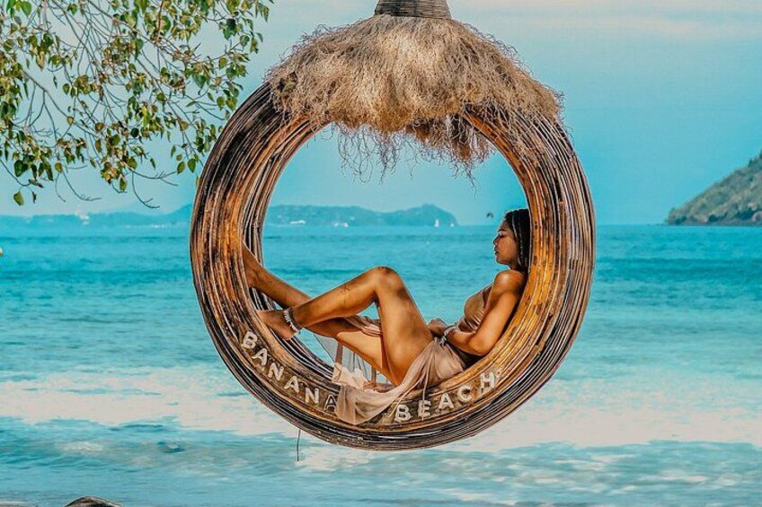 A person relaxing in a circular hammock with 'BANANA BEACH' written on it, by the sea. 5