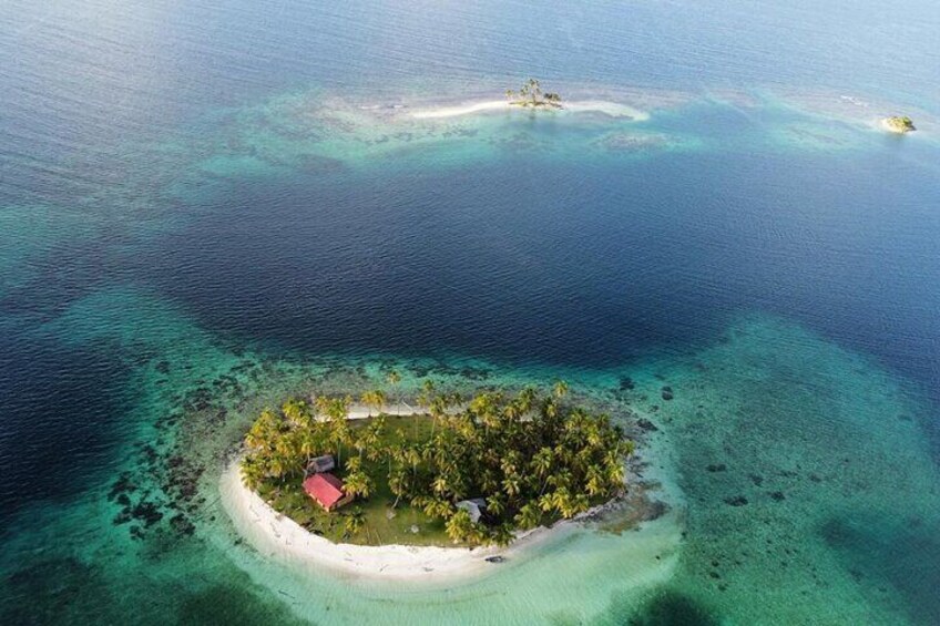 An aerial view of a small island with clear turquoise waters and a red-roofed building surrounded by lush greenery. 4