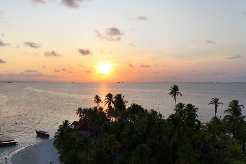 A sunset over a calm sea with palm trees and a boat on the shore. 5