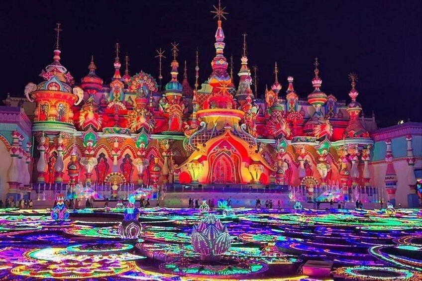 A brightly lit, colorful building with multiple domes and spires, surrounded by a water fountain display. 3