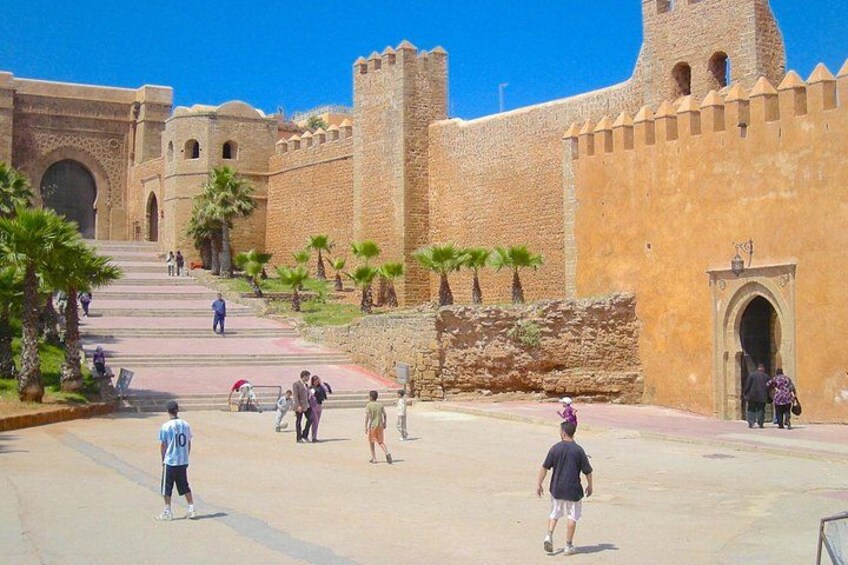 A historical fort with a large gate, palm trees, and people walking around. 3