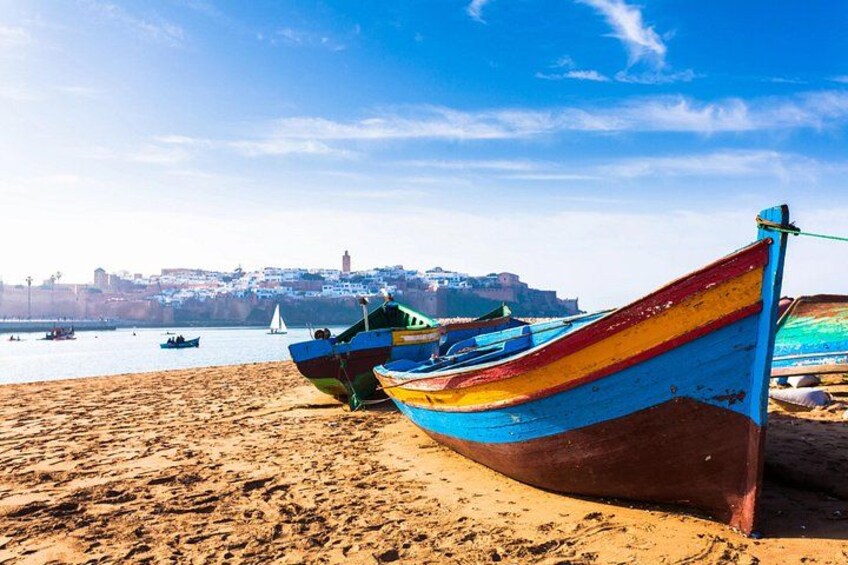 A sandy beach with colorful boats and a distant cityscape. 1
