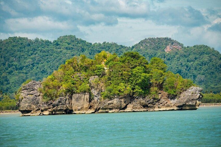 Una isla rocosa con follaje verde exuberante, rodeada de aguas turquesas tranquilas y una montaña boscosa al fondo. 2