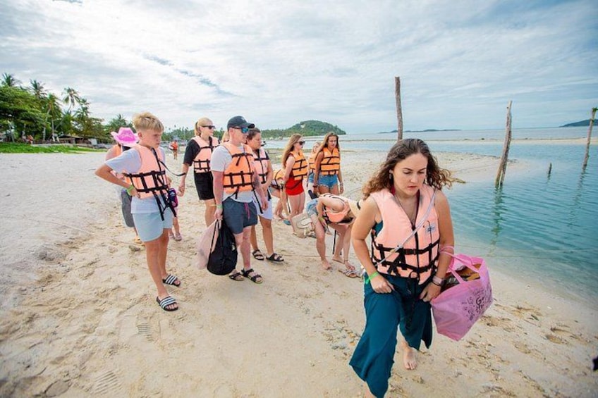 Un grupo de personas en la playa, algunas usando chalecos salvavidas, con un cielo despejado y un mar tranquilo al fondo. 3