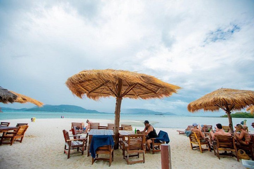 Un restaurante junto a la playa con mesas de madera y sombrillas de paja. 4