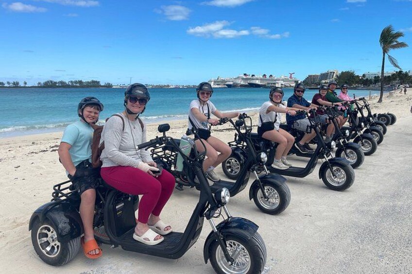 People riding electric scooters on a beach with the ocean and palm trees in the background. 5