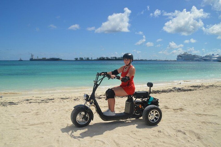A person riding an electric scooter on a sandy beach with a clear blue sky and calm sea in the background. 4