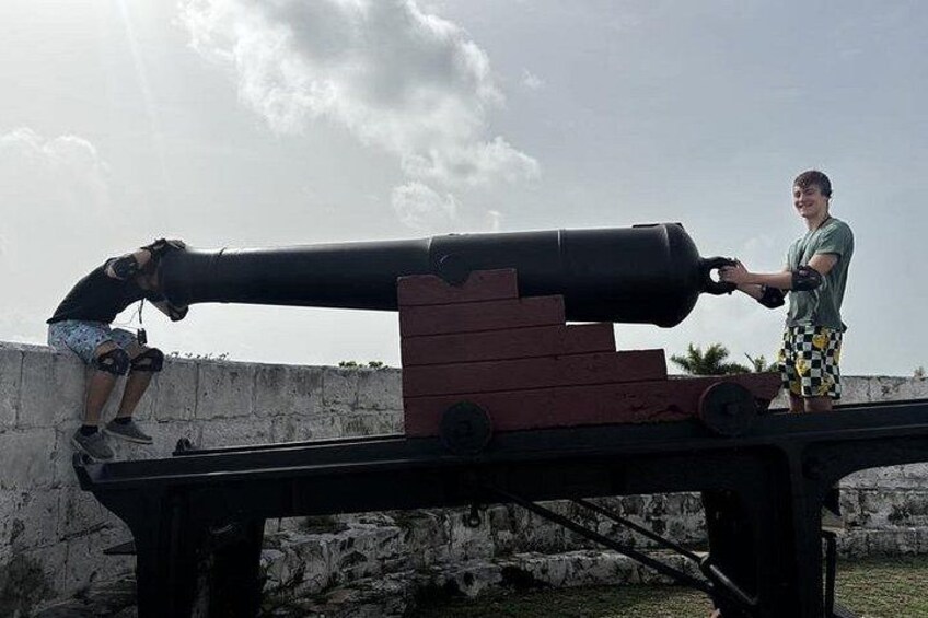 A large cannon on a platform with a person sitting on a wall and another person standing next to it. 2