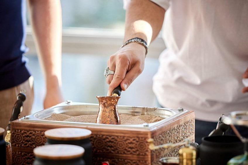 A person pouring coffee from a traditional copper pot into a glass. 1