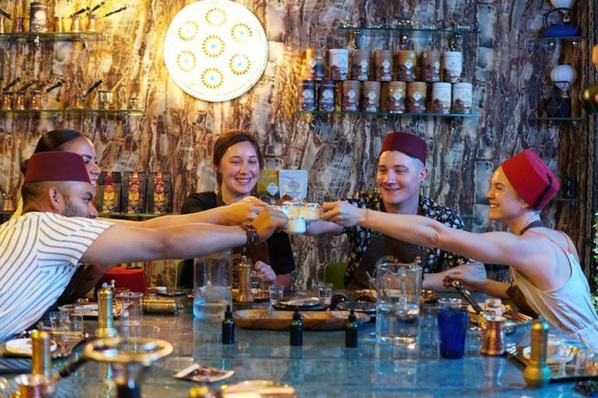 A group of people toasting at a bar with a marble wall and shelves of bottles in the background. 4