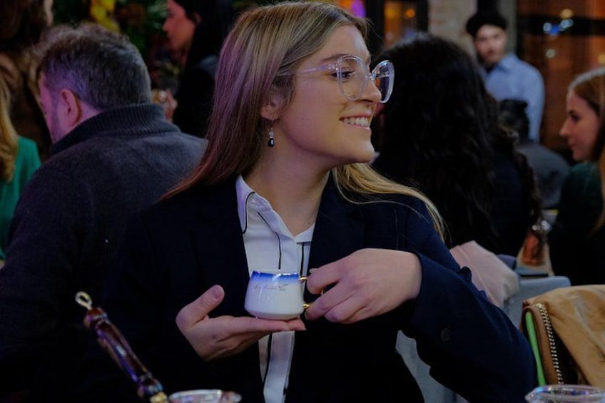 A person holding a small object, possibly a container or a box, at a social event with other people in the background. 5