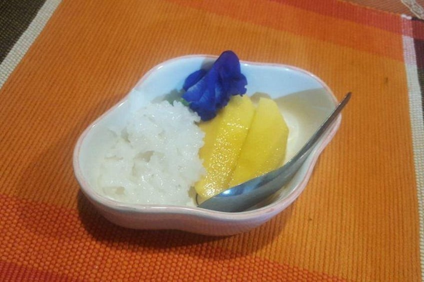 Een schaal witte rijst, geel fruit en een blauwe bloem op een oranje placemat. 3