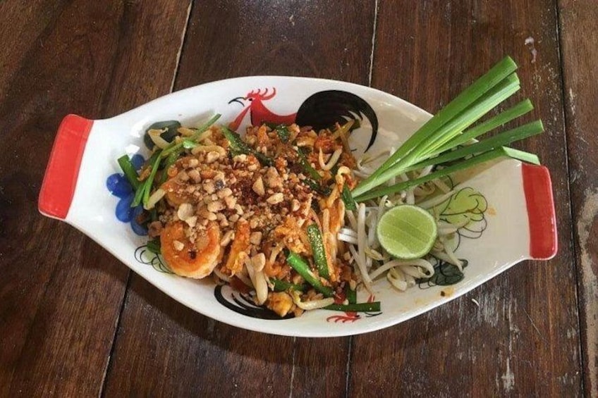 Een bord Pad Thai met noedels, garnalen en groenten op een houten tafel. 4