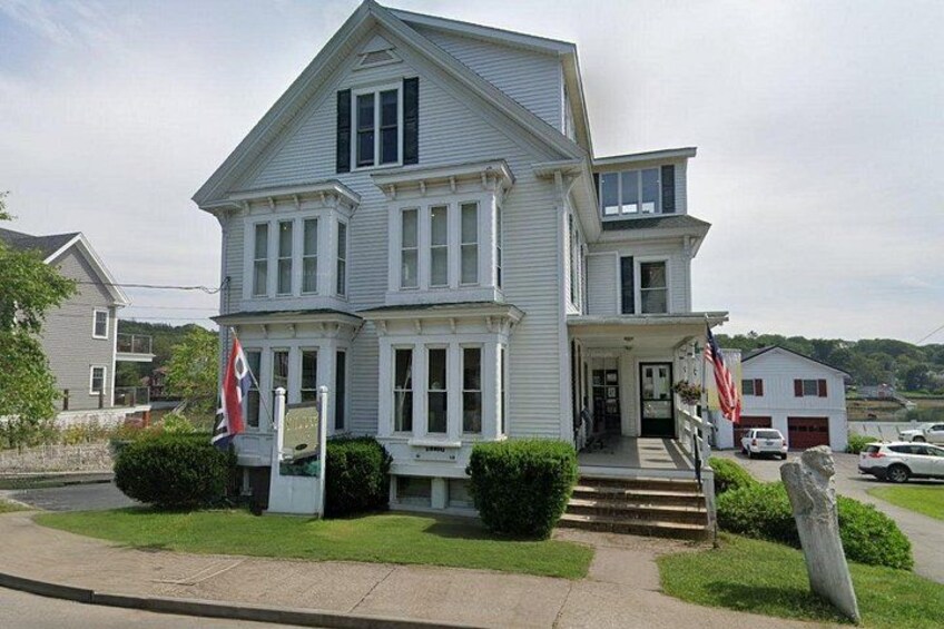 A white two-story building with a porch, American flags, and a small flagpole. 2