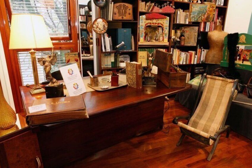 A wooden desk with a lamp, a chair, and a bookshelf filled with books and decorative items. 5