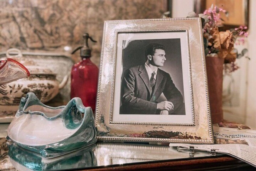 A vintage photograph in a decorative frame, a glass pitcher, and a red bottle on a reflective surface. 2