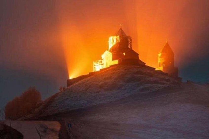A snow-covered hill with a church and a bell tower illuminated by a bright light. 4