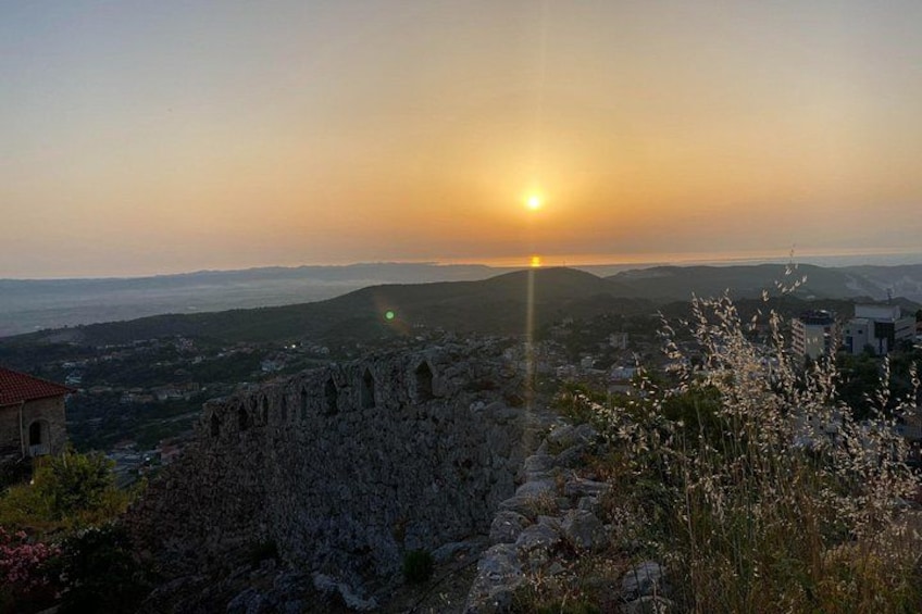 A sunset over a mountainous landscape with ruins and a distant city. 3