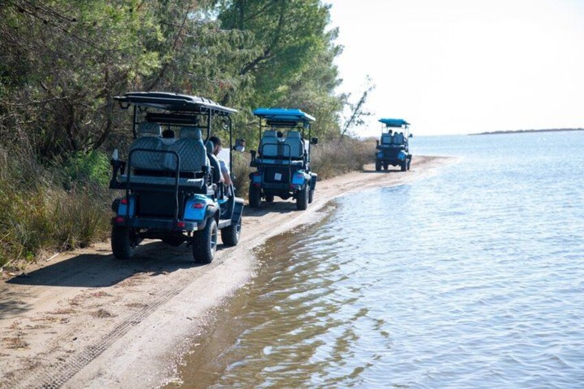 Three golf carts parked by a sandy beach with water on the right. 2