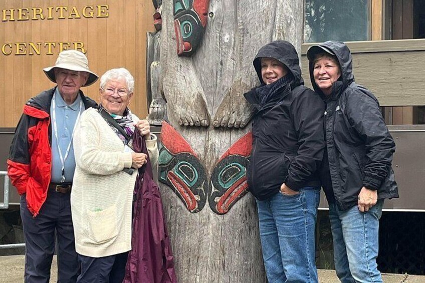 Un tótem de madera con figuras pintadas, un cartel del Centro del Patrimonio y personas de pie al frente. 5