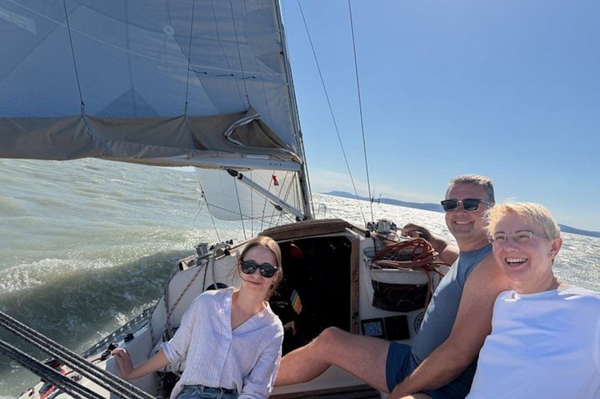 A sailboat with three people on board, a clear sky, and calm waters. 4