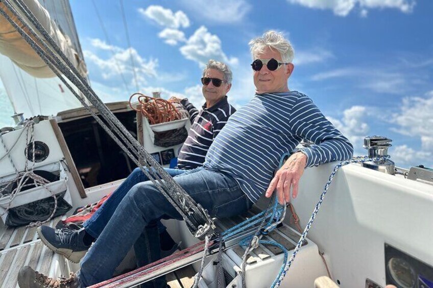 Two people on a sailboat, one sitting on the deck and the other leaning on the railing. 2
