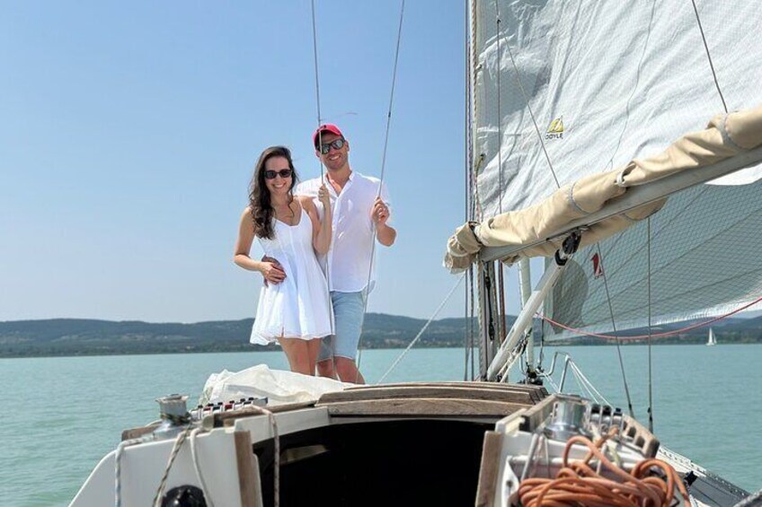A couple on a sailboat with a calm sea and distant hills in the background. 3