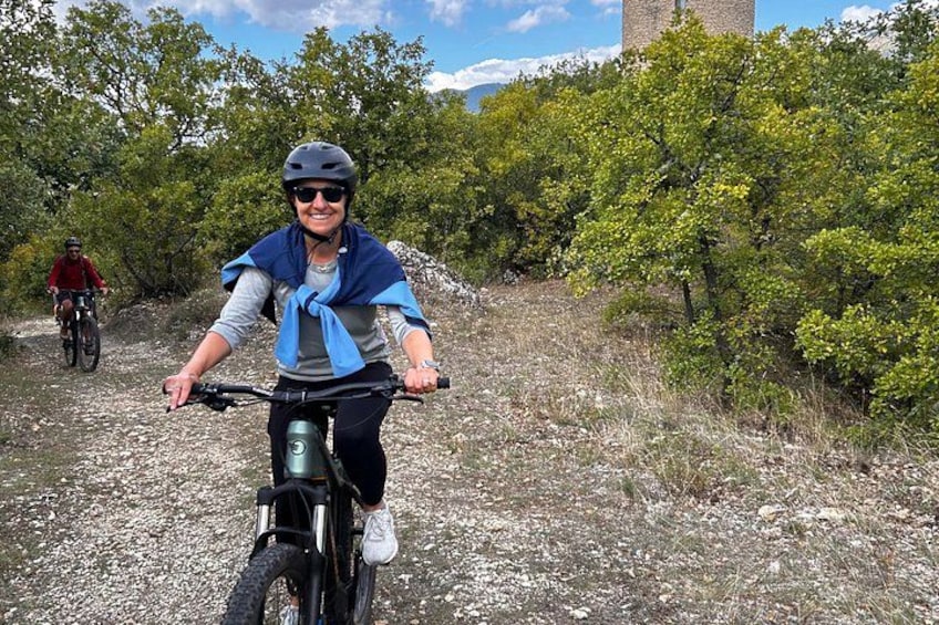 A person riding a bicycle on a gravel path with trees and a building in the background. 5