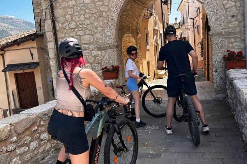 Three people on bicycles in a narrow stone pathway with buildings on either side. 4