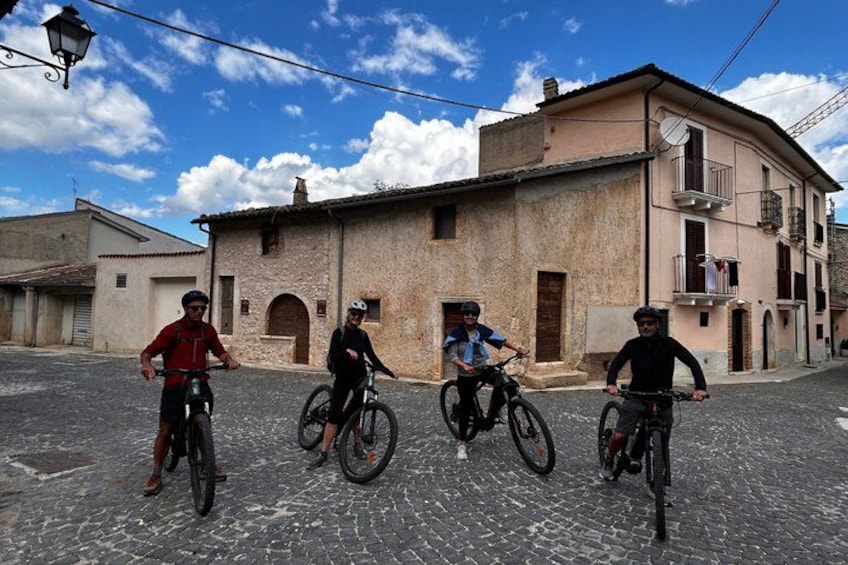 Three cyclists on a cobblestone street in front of a building with a balcony. 2