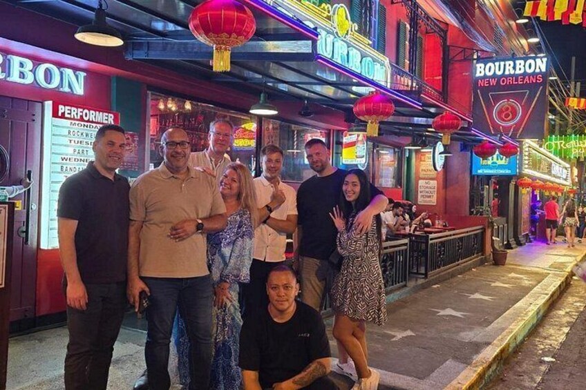 A group of people posing in front of a brightly lit bar with neon signs, including one for Bourbon New Orleans. 2