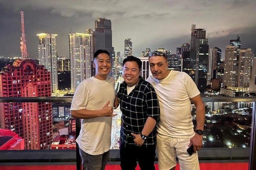 Three individuals standing on a balcony with a city skyline in the background. 5