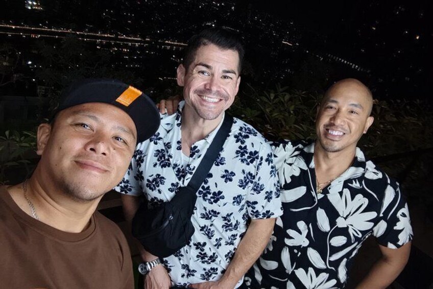 Three people standing outdoors at night with city lights in the background. 5