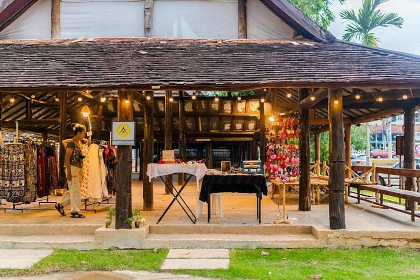 A rustic wooden structure with a covered outdoor market area, a mannequin dressed in traditional attire, and a table with items on display. 4