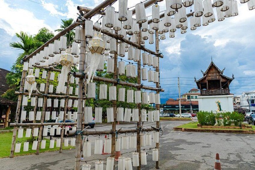 A bamboo structure with hanging lanterns, a traditional building, and a modern building in the background. 3