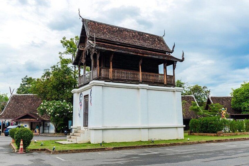 A traditional wooden structure with a balcony, surrounded by modern buildings and greenery. 2